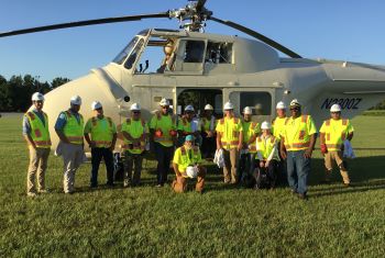 Newcomb Team members posing in front of a helicopter